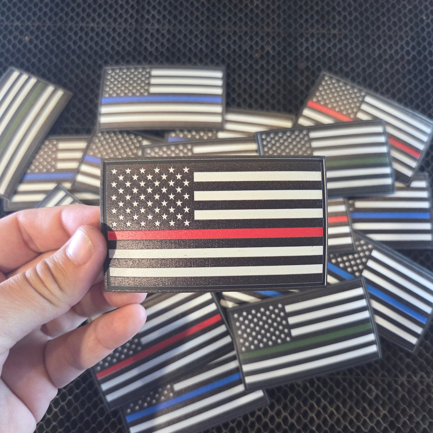 Hand holding a thin red line American flag patch with other similar patches in the background.