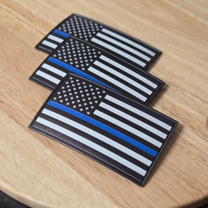 Three flag patches with blue, white, and black stripes on a wooden surface