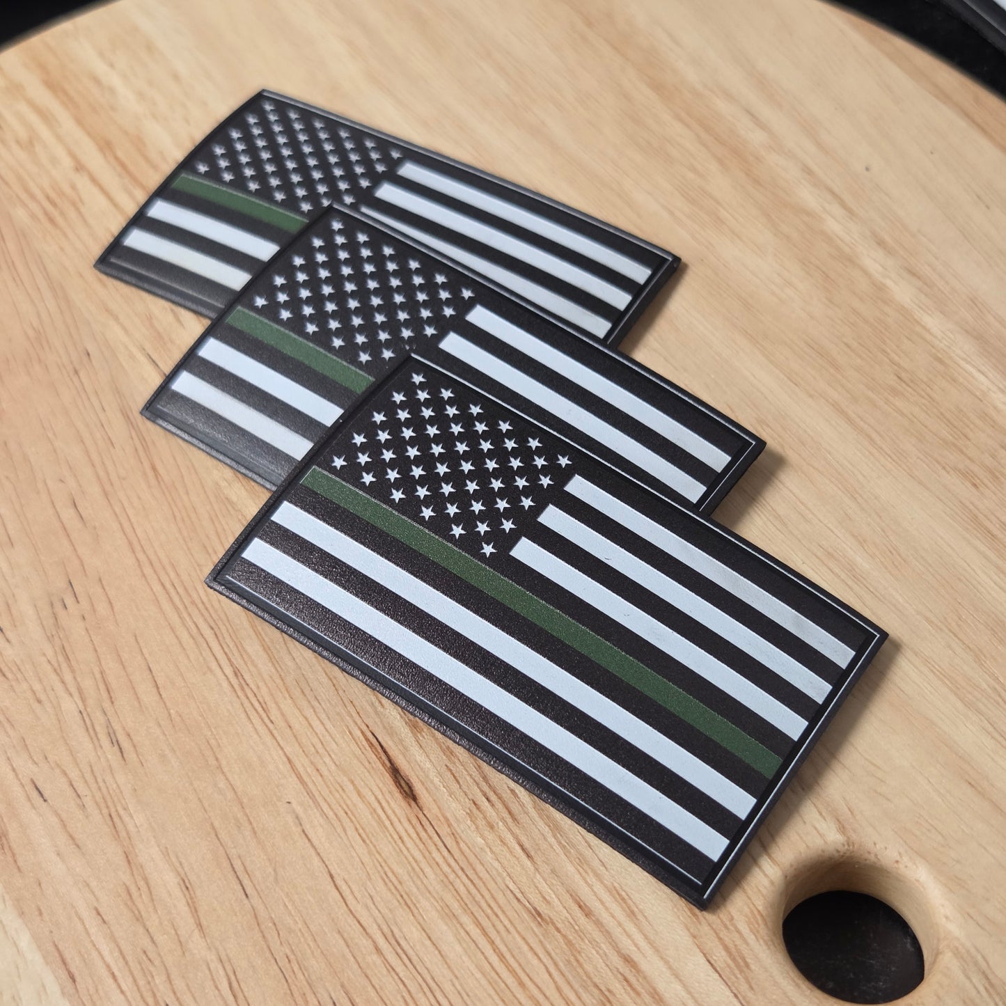 Three American flag patches with thin green line on a wooden surface